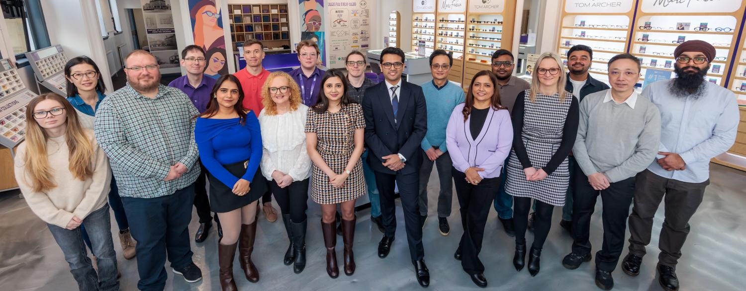 A group photo of the Specscart team posing outside a Specscart retail storefront with a purple door and classic stone facade.