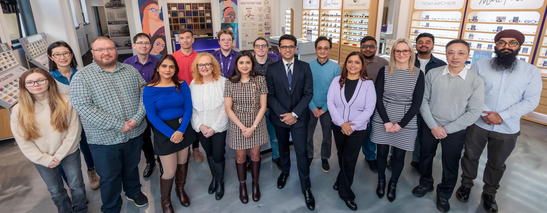 A group photo of the Specscart team posing outside a Specscart retail storefront with a purple door and classic stone facade.