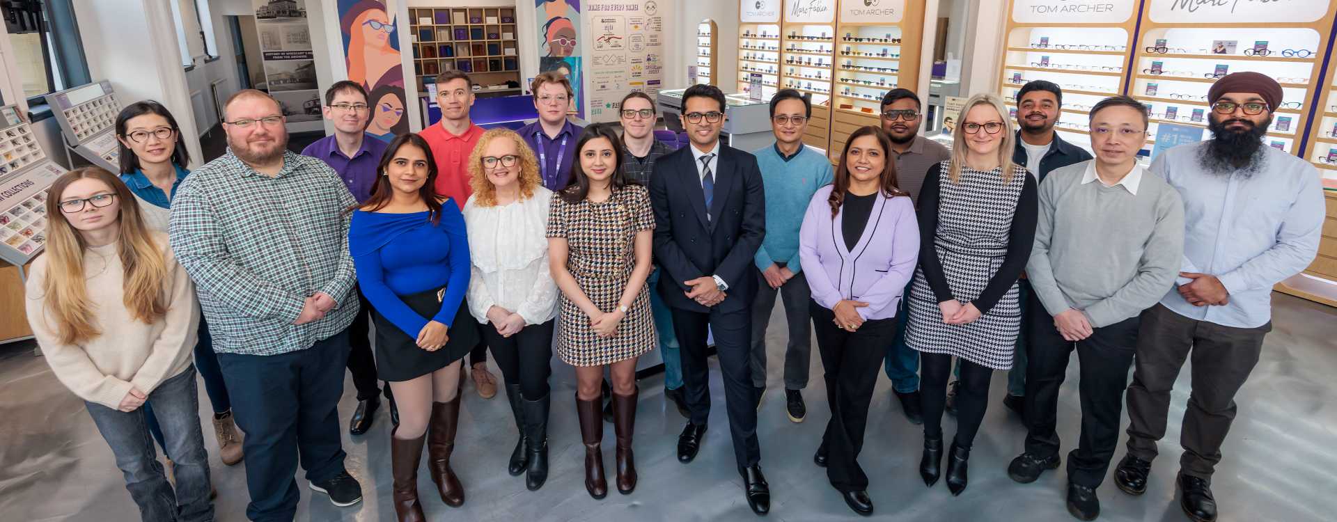 A group photo of the Specscart team posing outside a Specscart retail storefront with a purple door and classic stone facade.