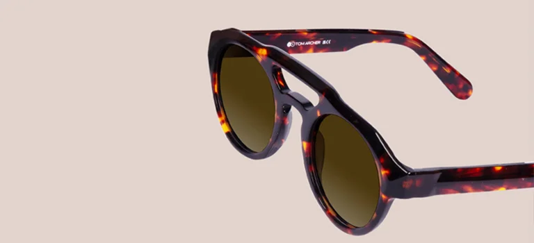 Double Bridge Sunglasses Stylish round tortoiseshell sunglasses featuring a unique double bridge design and dark lenses, showcased against a minimalist beige background.