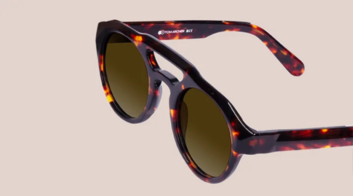 Double Bridge Sunglasses Stylish round tortoiseshell sunglasses featuring a unique double bridge design and dark lenses, showcased against a minimalist beige background.